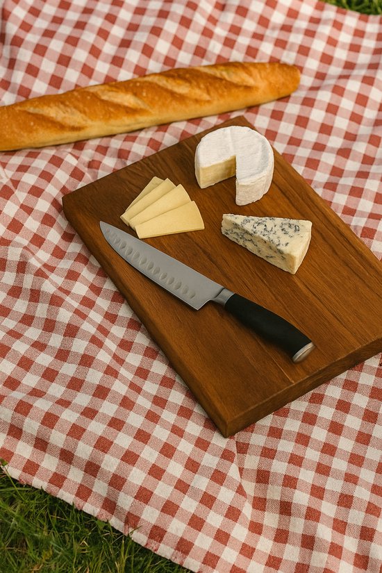 Basic Culinair teakhouten snijplank met koksmes, kaas en stokbrood op een picknickkleed in het gras