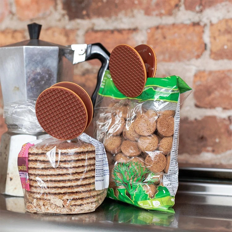 Kikkerland Bagclips Stroopwafel - 4 stuks, sfeerbeeld op een tas stroopwafels, tegen een bakstenen muur