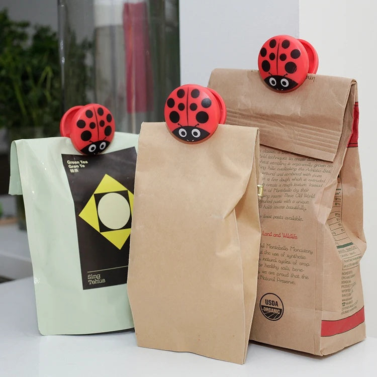 Kikkerland Bagclips Lieveheersbeestje - 6 stuks, sfeerbeeld op papieren zakken met koffie en thee