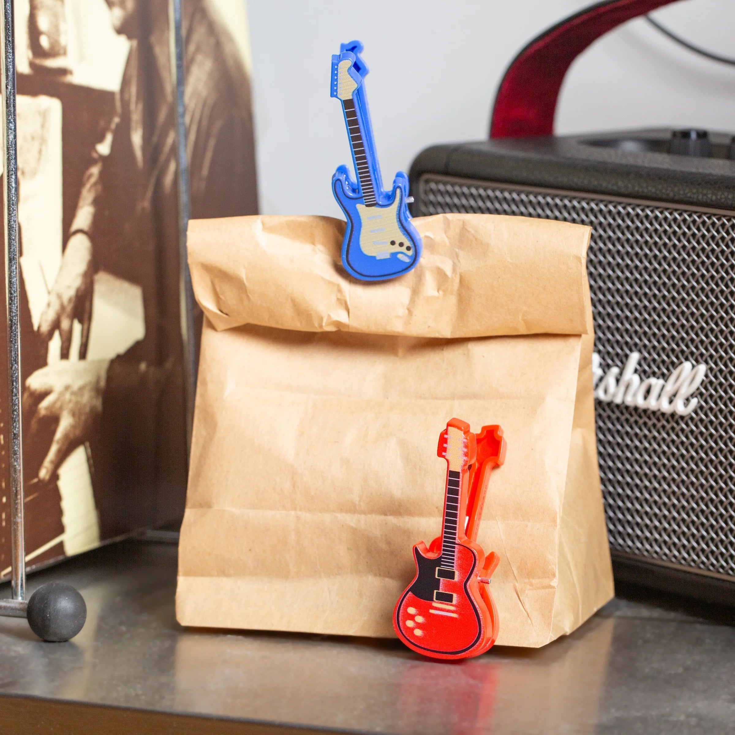Kikkerland Bagclips Gitaren - 4 stuks, sfeerbeeld op een papieren zak naast een speaker