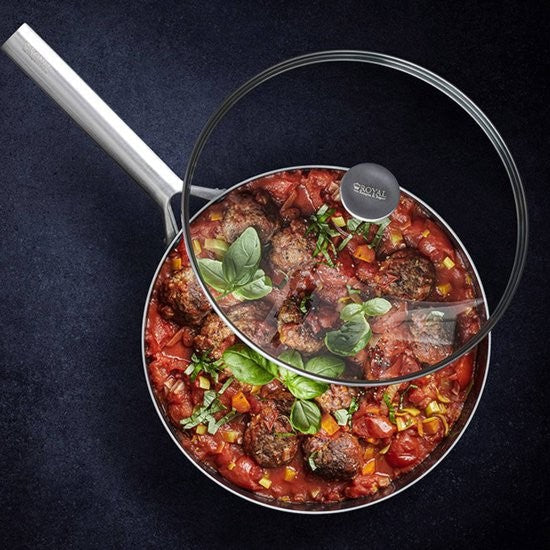 Royal Van Kempen hapjespan gevuld met tomatensaus, gehaktballetjes en verse basilicum, het glazen deksel met roestvrijstalen rand en knop met 'Royal'-logo leunt schuin op de pan tegen een donkere ondergrond.