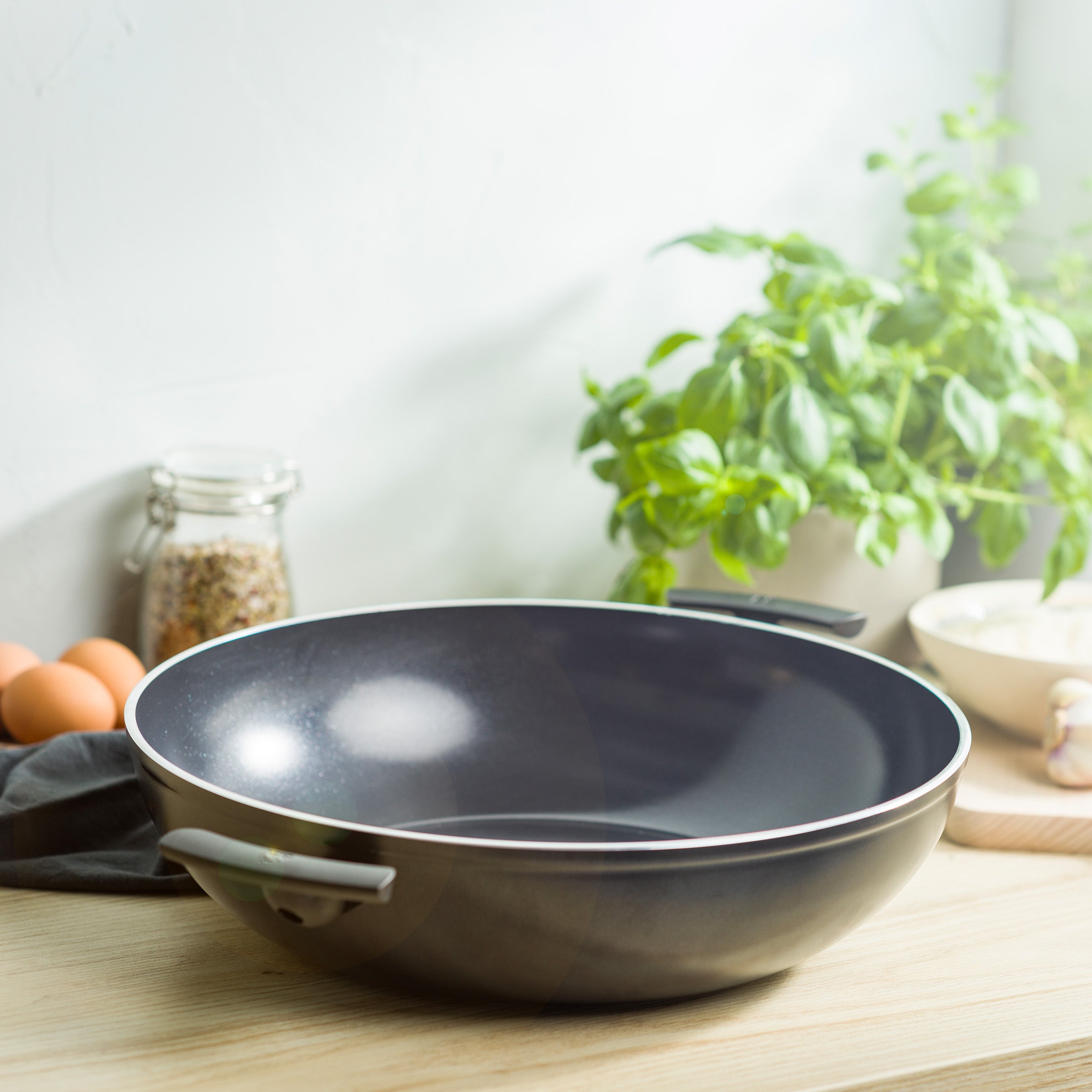 Zwarte BK Easy Induction wadjan op een houten aanrecht met basilicum en eieren ernaast.