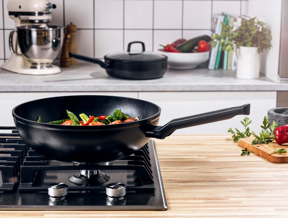Zwarte BK Easy Induction wokpan met roergebakken groenten op een gasfornuis.