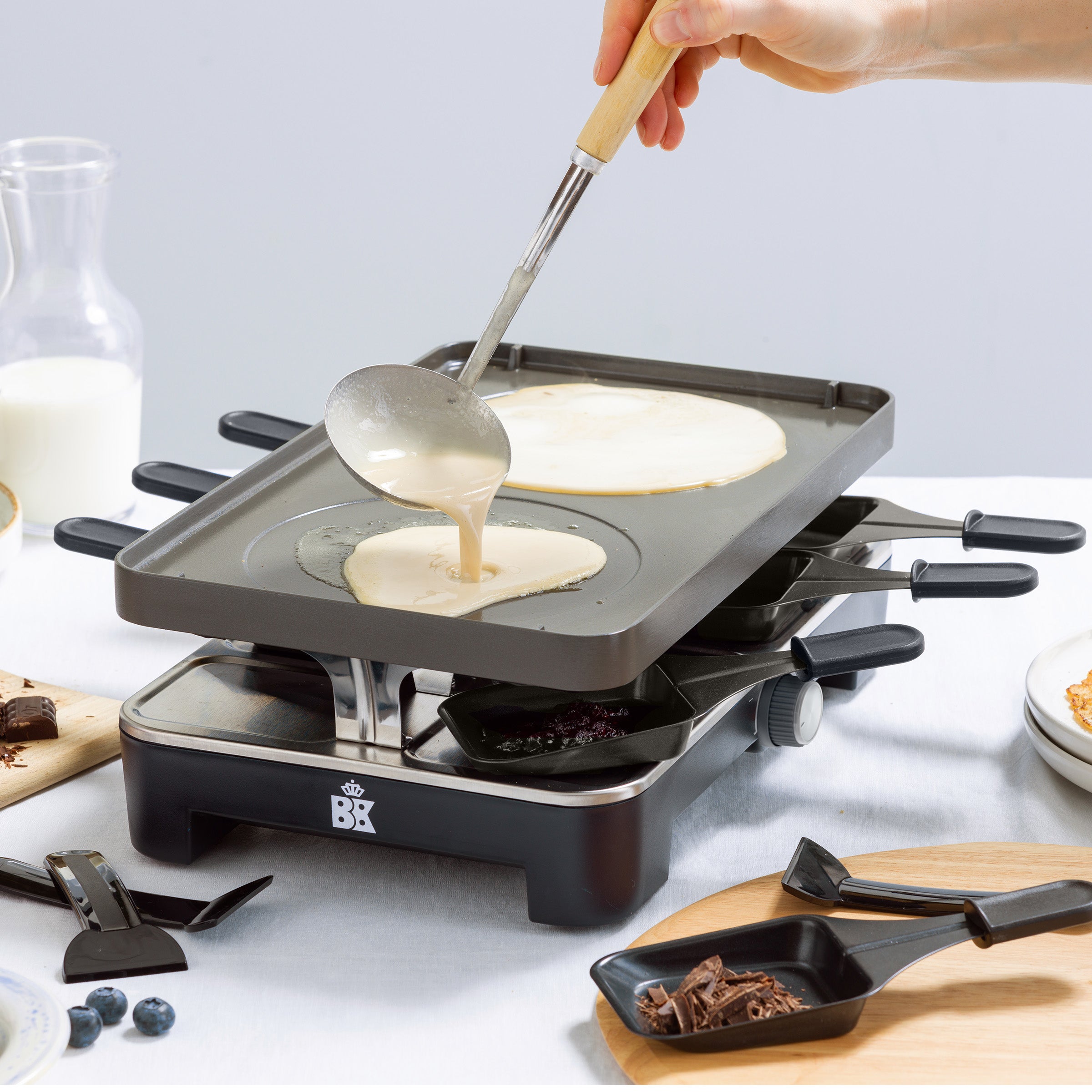 Hand giet pannenkoekbeslag op de omgekeerde bakplaat van de zwarte BK Connect raclette.