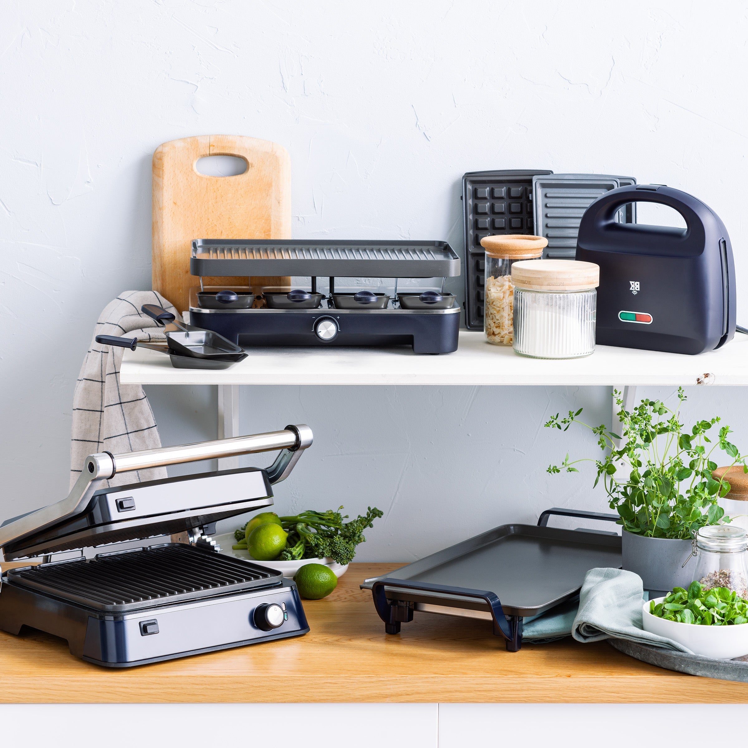 Collectie zwarte BK Connect apparaten, waaronder raclette en bakplaat, op twee planken.
