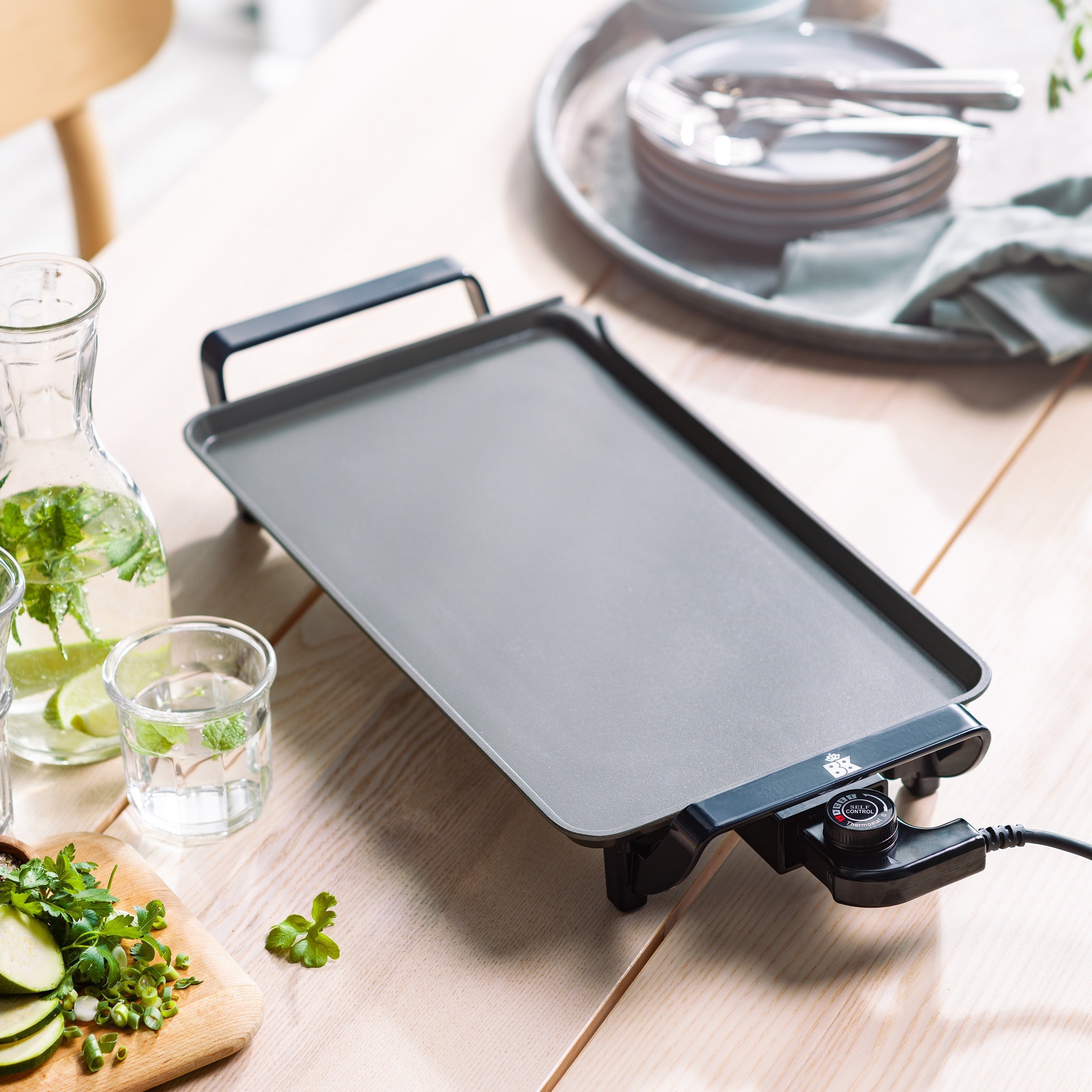 Zwarte BK Connect bakplaat op een houten tafel, met karaf en borden op de achtergrond.