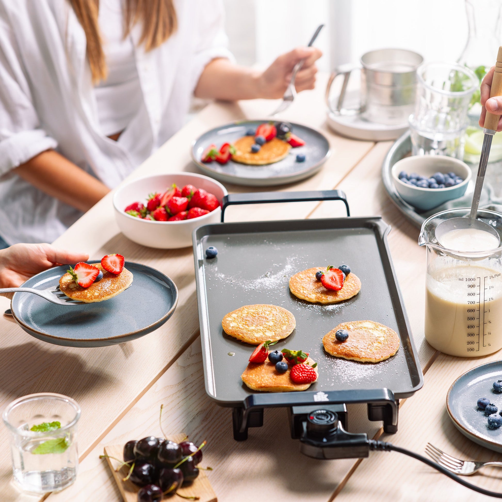 Zwarte BK Connect bakplaat met kleine pannenkoekjes en vers fruit op een gedekte tafel.