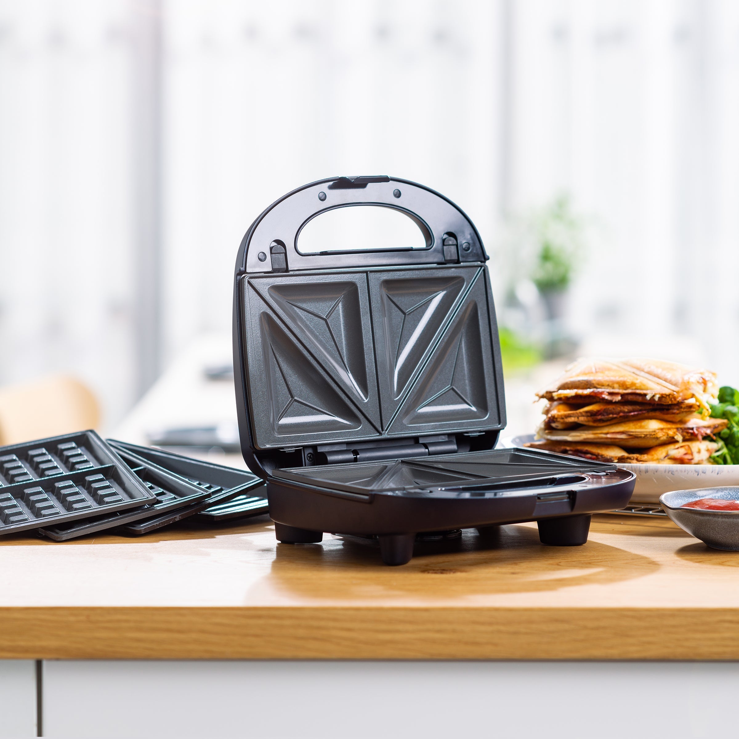 Zwarte BK Connect 3-in-1 grill geopend op een aanrecht, met tosti's en wafelplaten ernaast.