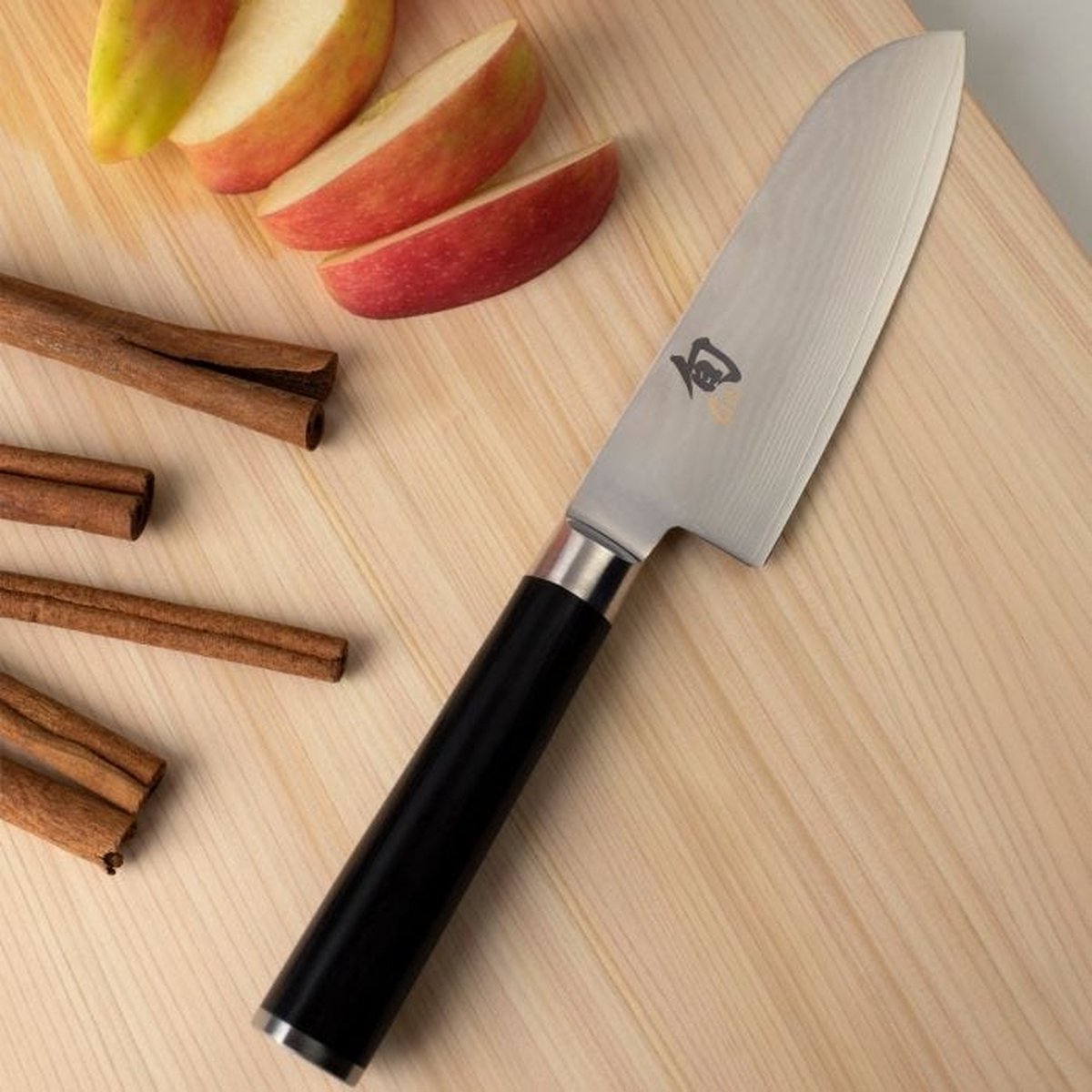 Kai Shun Classic Santoku First Touch - 14 cm, op een houten snijplank naast appelpartjes en kaneelstokjes