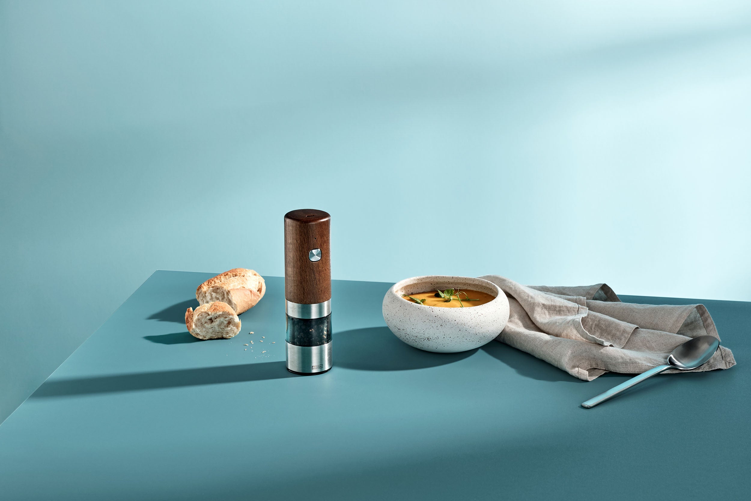 Twee AdHoc elektrische houten molens op een blauwe tafel bij een kom soep, brood en een lepel