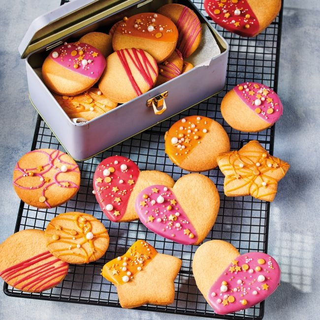 Versierde koekjes in verschillende vormen op een taartrooster en in een blikken trommel