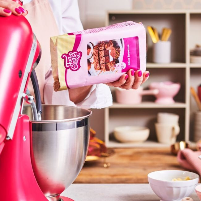Hand houdt een pak FunCakes Mix voor Fudge Brownie boven een mengkom