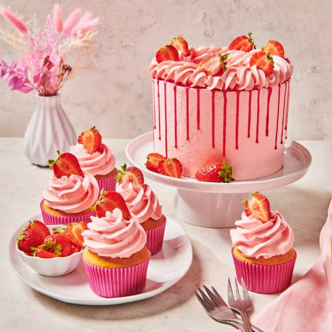 Aardbeientaart met roze botercrème en cupcakes met aardbeien op tafel