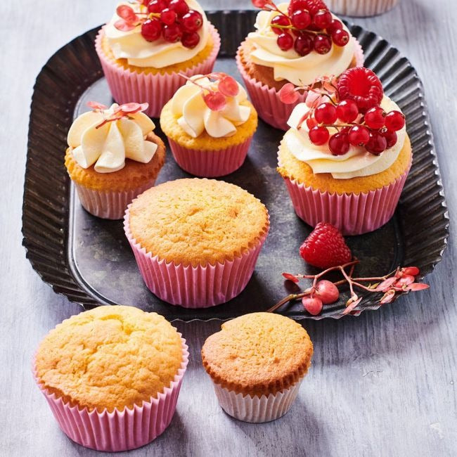Cupcakes met slagroom, rode bessen en framboos op een dienblad naast losse cakejes zonder topping