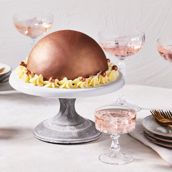 Bolvormige taart met bronskleurig glitterglazuur, botercrème rozetten en chocoladeparels op een taartstandaard
