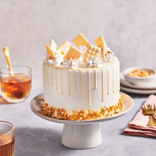 Taart met witte drip en witte chocoladedecoraties op een taartplateau
