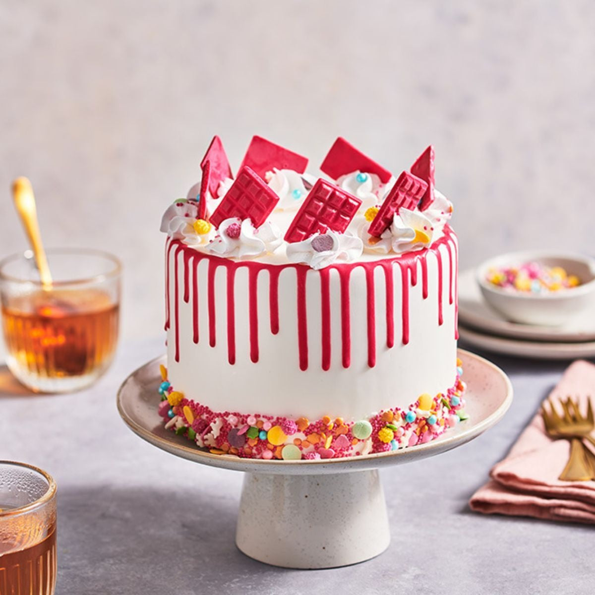 Taart met rode drip, rode chocoladeplakken en gekleurde sprinkles onderaan op een taartplateau