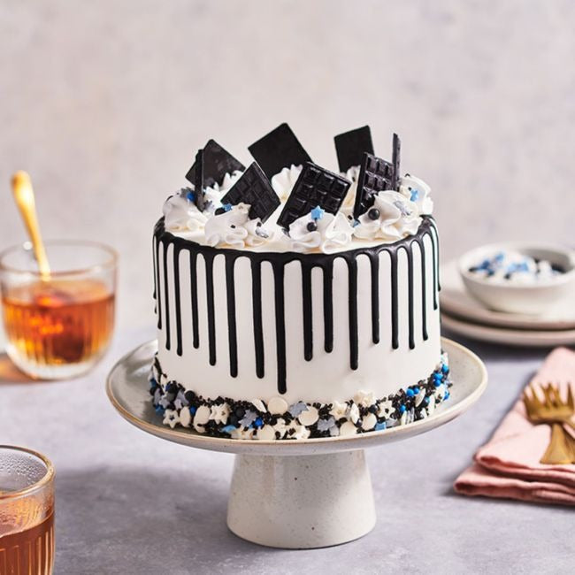 Taart met zwarte drip, zwarte chocoladeplakken en zwart-witte sprinkles onderaan op een taartplateau