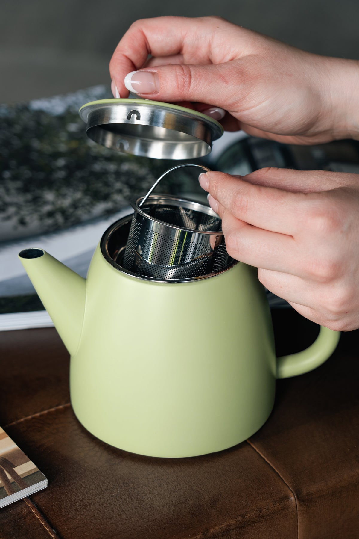 Handen tillen het deksel op en houden het geperforeerde zeefmandje boven de opening van de lichtgroene theepot