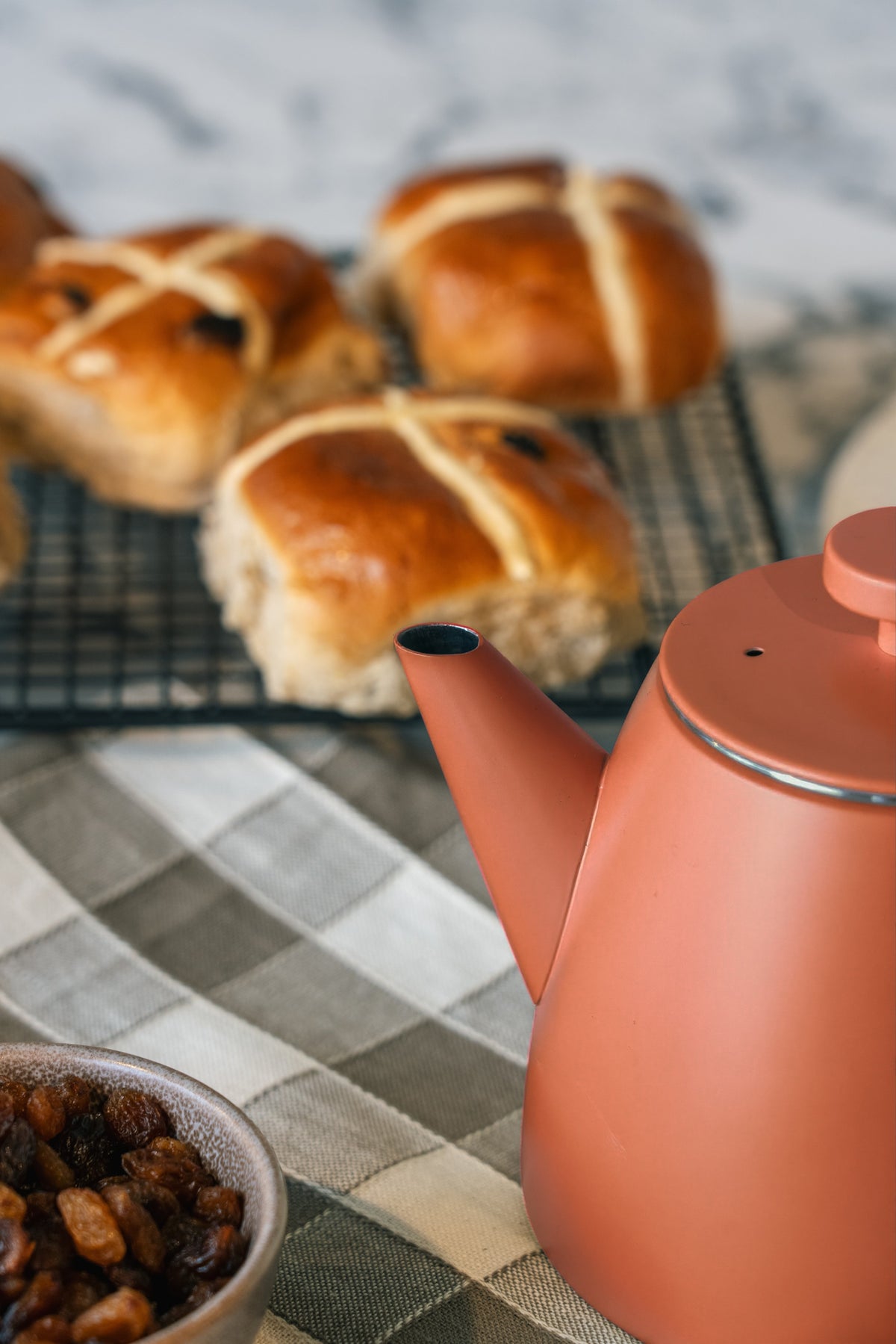 Tuit en dekselrand van de roodoranje theepot van dichtbij, met broodjes op een rooster en rozijnen in een kommetje