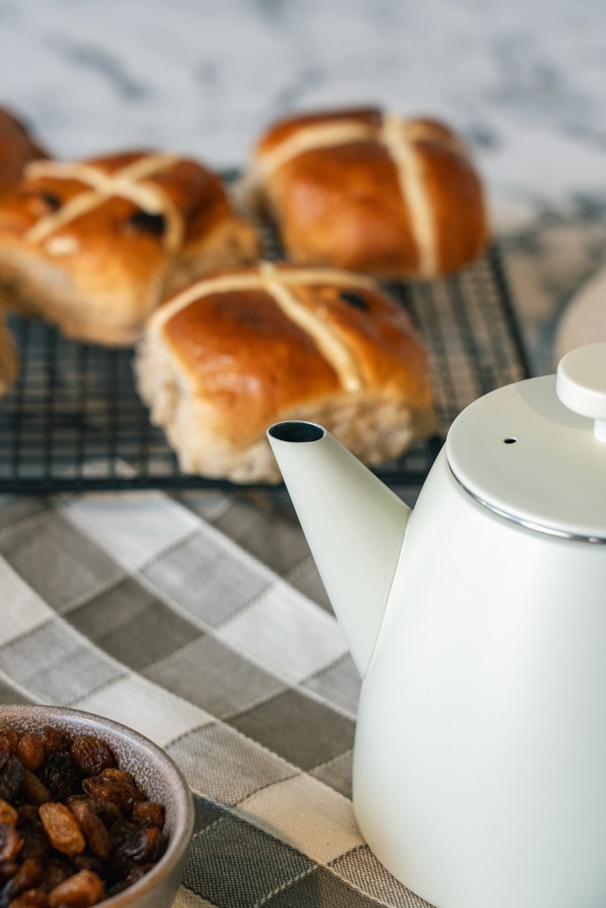 Tuit en deksel van de witte theepot van dichtbij, met een metalen randje rond het deksel en een kommetje rozijnen