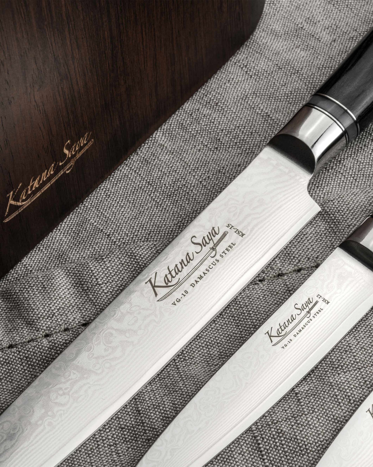 Close-up van Damascus-lemmeten met Katana Saya-gravure op grijze linnen doek naast het donkere houten blok