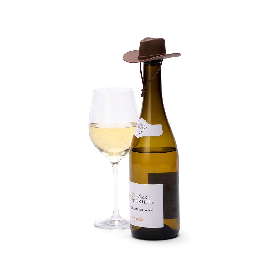 Fles witte wijn met een donkerbruine hoedstopper en een gevuld glas ernaast op een witte achtergrond
