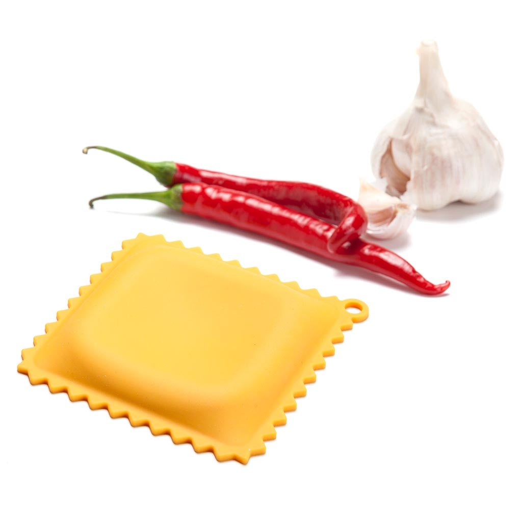 Gele ravioli-lepelhouder naast twee rode pepers en een bol knoflook op een witte achtergrond