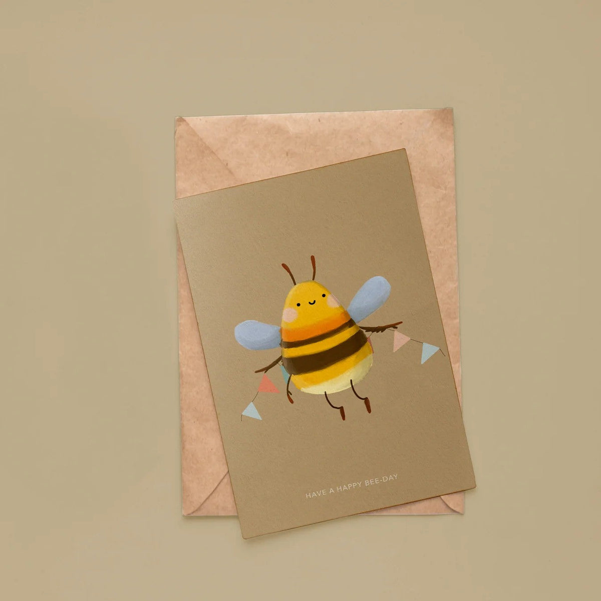 Wenskaart van Depre Design met een geïllustreerde bij en vlaggenlijn, op een kraft envelop tegen een beige achtergrond.