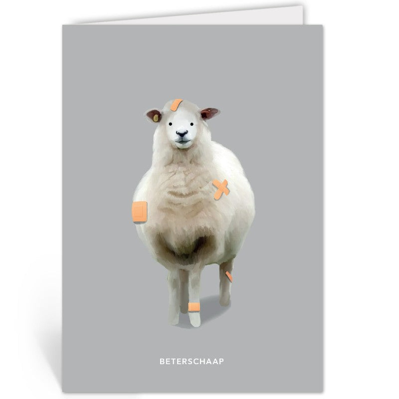 Beterschapskaart met een schaap vol pleisters, liggend op een kraftpapieren envelop tegen een grijsbruine achtergrond.