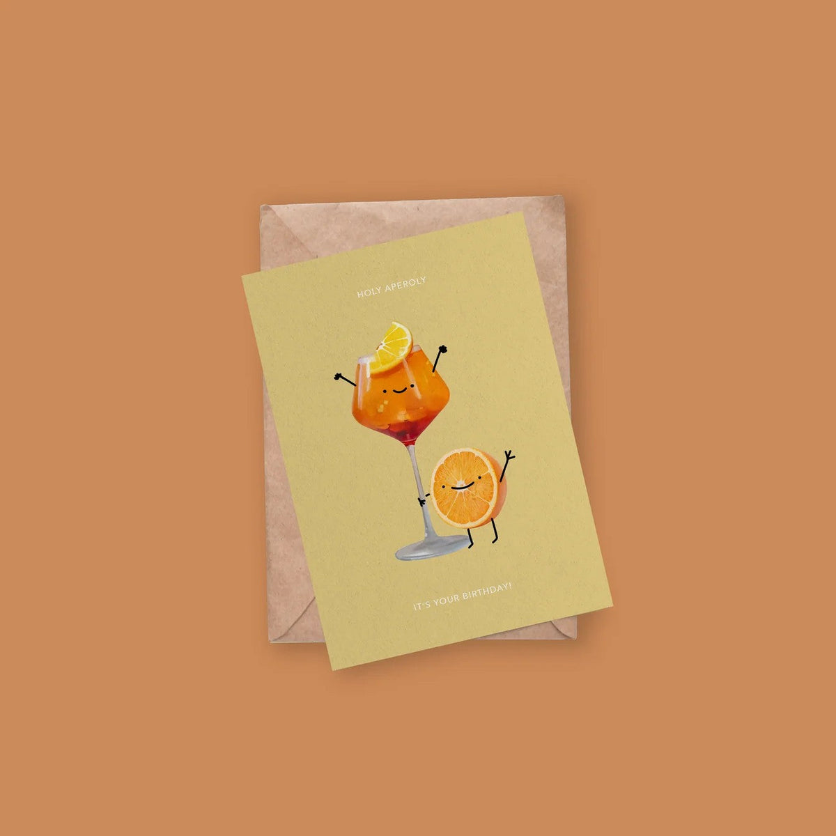 Wenskaart 'Holy Aperoly' van Depre Design op gele achtergrond, met een illustratie van een Aperol Spritz en een dansend sinaasappelschijfje, kraftpapieren envelop eronder.