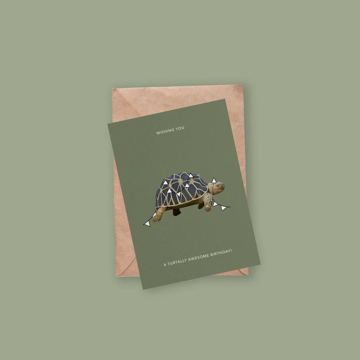 Wenskaart met schildpad-illustratie liggend op een kraft envelop tegen groene achtergrond