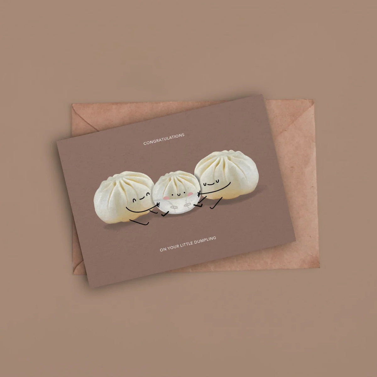 Wenskaart met drie knuffelende dumplings, plat neergelegd op een kraftpapieren envelop tegen een bruine achtergrond