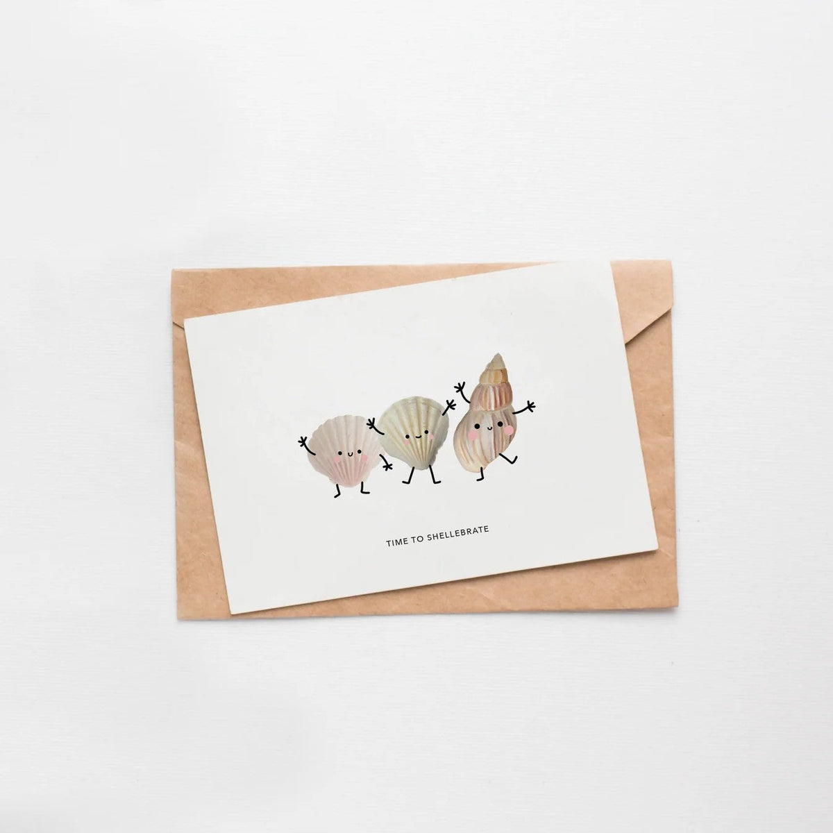Wenskaart met schelpjes-illustratie liggend op een kraft envelop tegen witte achtergrond