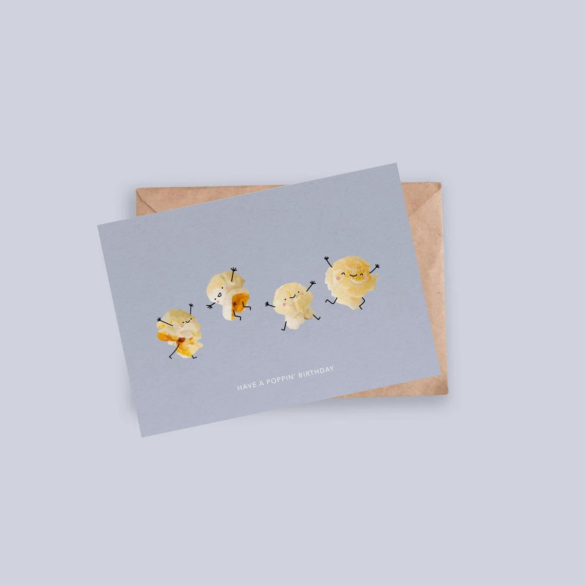 Lichtblauwe verjaardagskaart met dansende popcorn-illustraties, op een kraftpapieren envelop.