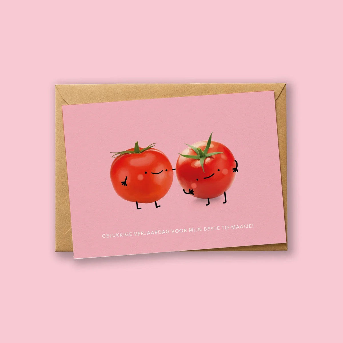 Wenskaart 'Gelukkige Verjaardag Voor Mijn Beste To-Maatje' van Depre Design op roze achtergrond, met twee illustraties van tomaatjes die een boks tegen elkaar geven, kraftpapieren envelop eronder.