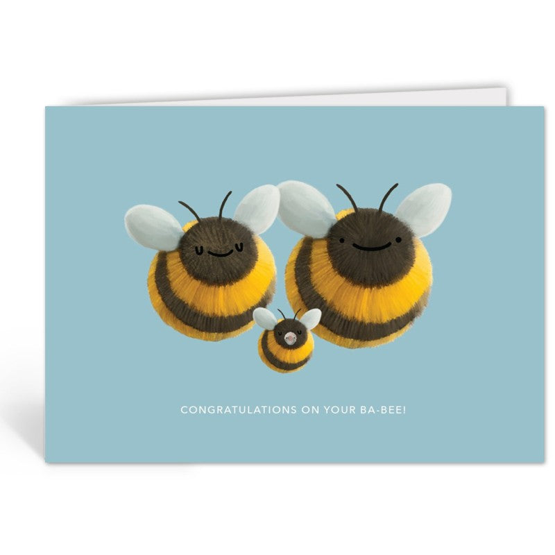 Opengevouwen felicitatiekaart 'Congratulations On Your Ba-Bee' van Depre Design met de hommelfamilie-illustratie, witte envelop op de achtergrond.