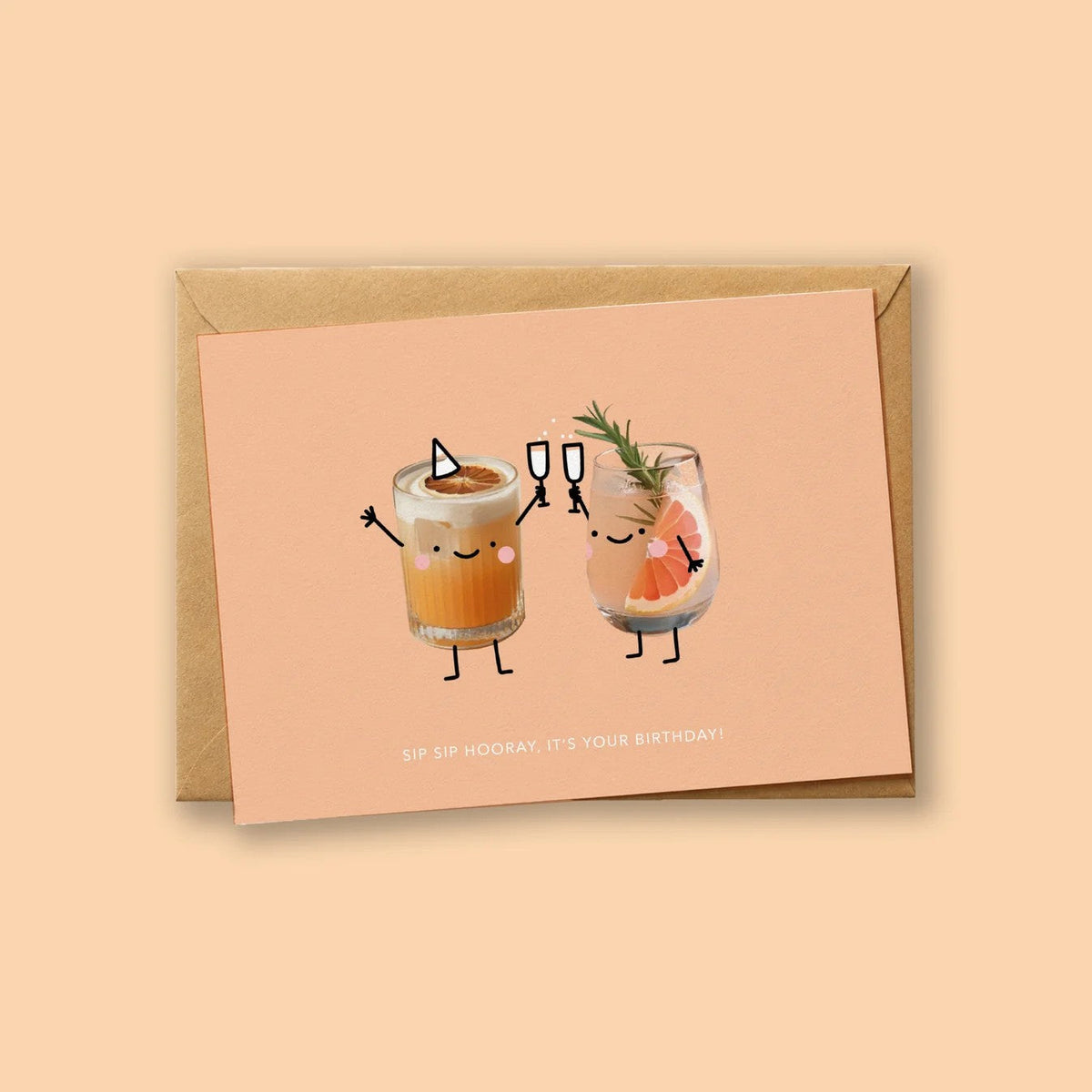 Wenskaart 'Sip Sip Hooray, It's Your Birthday' van Depre Design op perzikkleurige achtergrond, met twee illustraties van klinkende cocktailglazen, kraftpapieren envelop eronder.