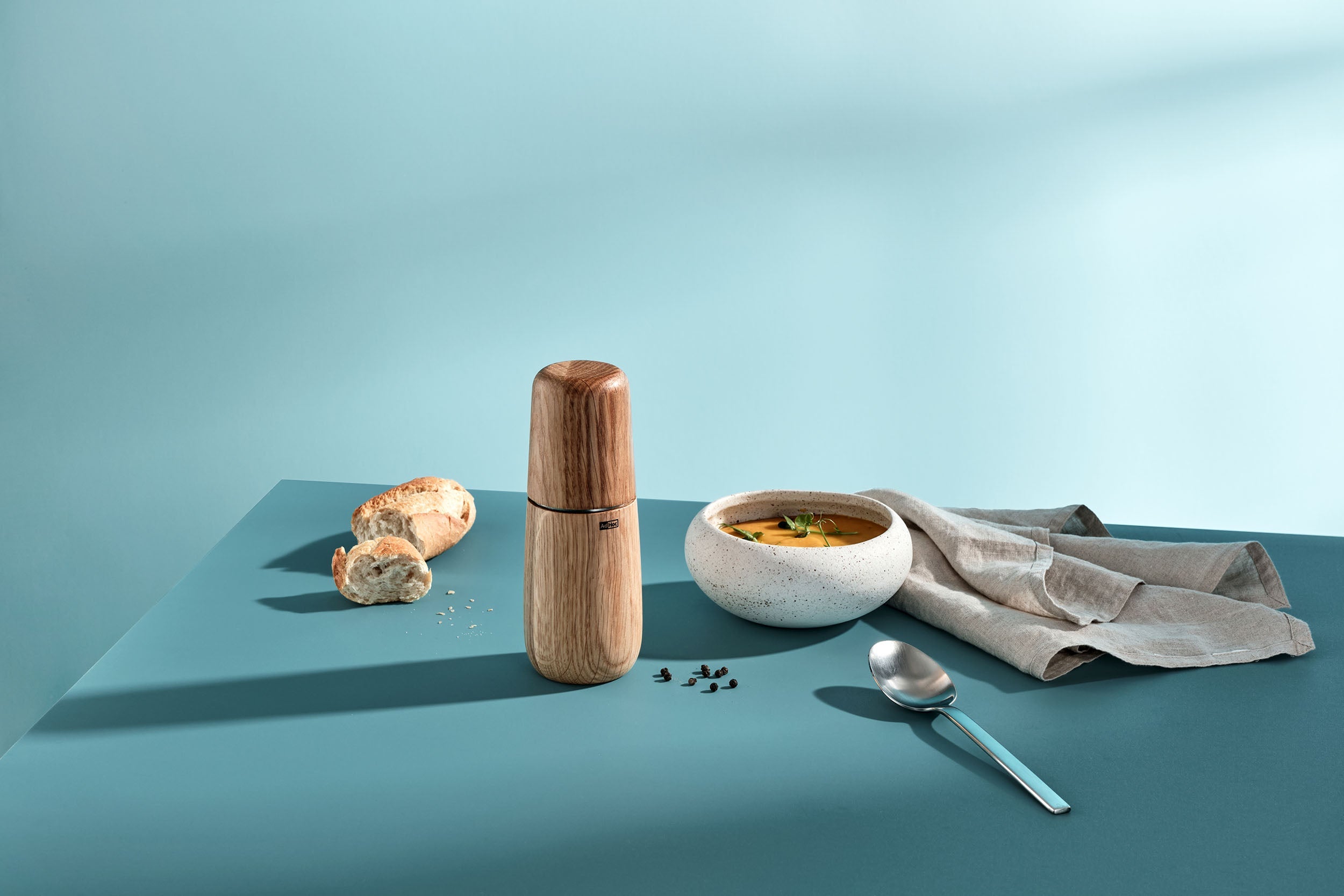 AdHoc Yono houten molen op een blauwe tafel bij een kom soep, brood en een lepel