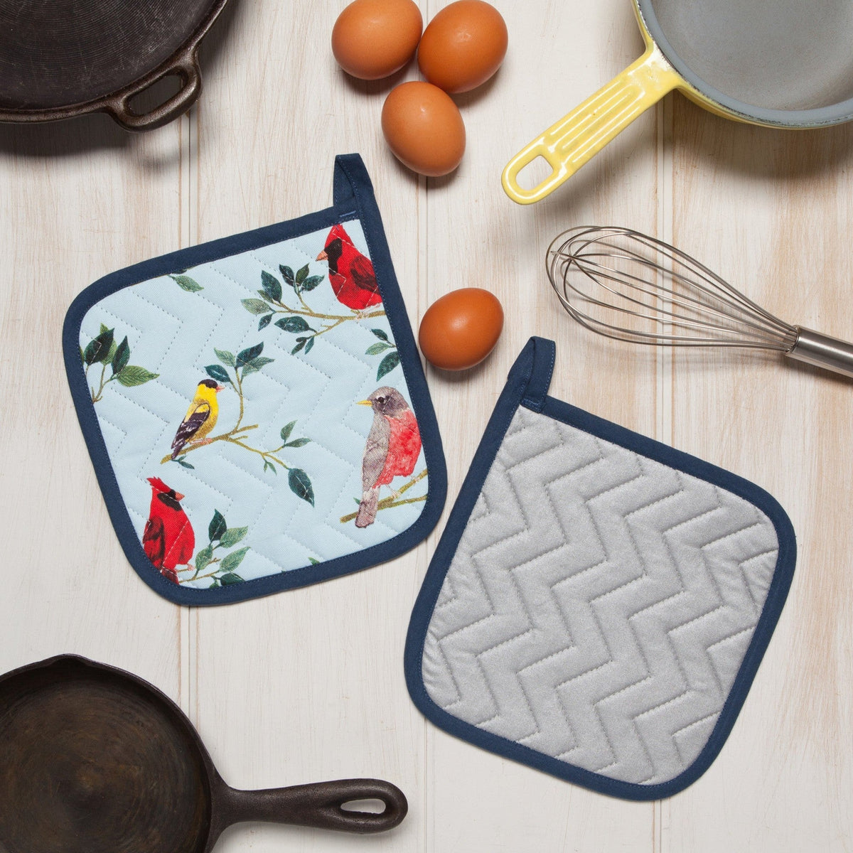 Voorkant met vogels en zilvergrijze achterkant met zigzagquilting naast eieren, een garde en gietijzeren pannen