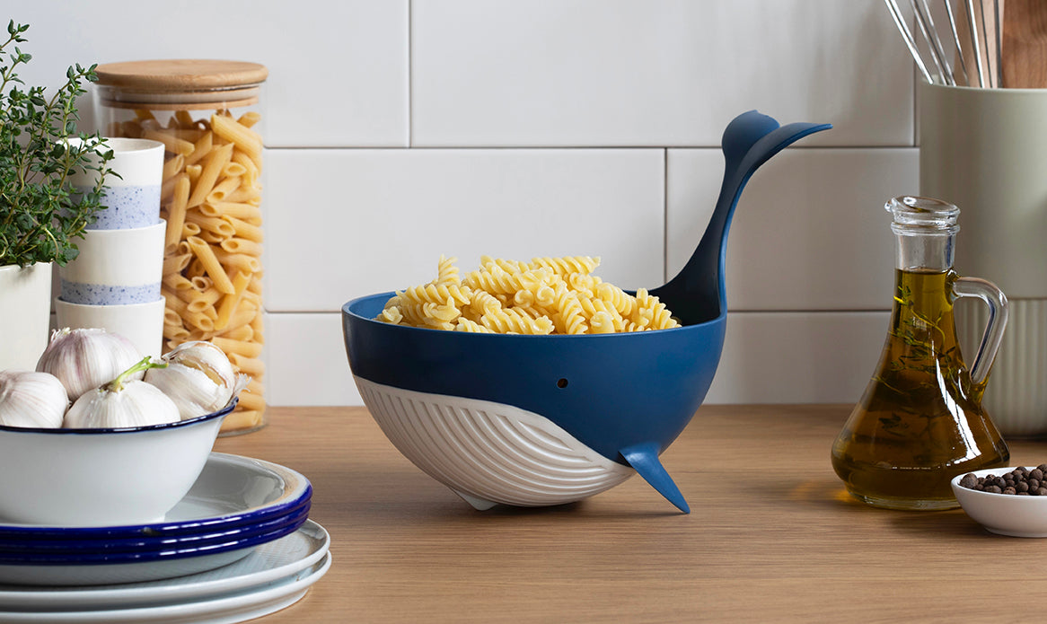 Pastail vergiet met pasta op een keukenblad tussen kruiden en olijfolie