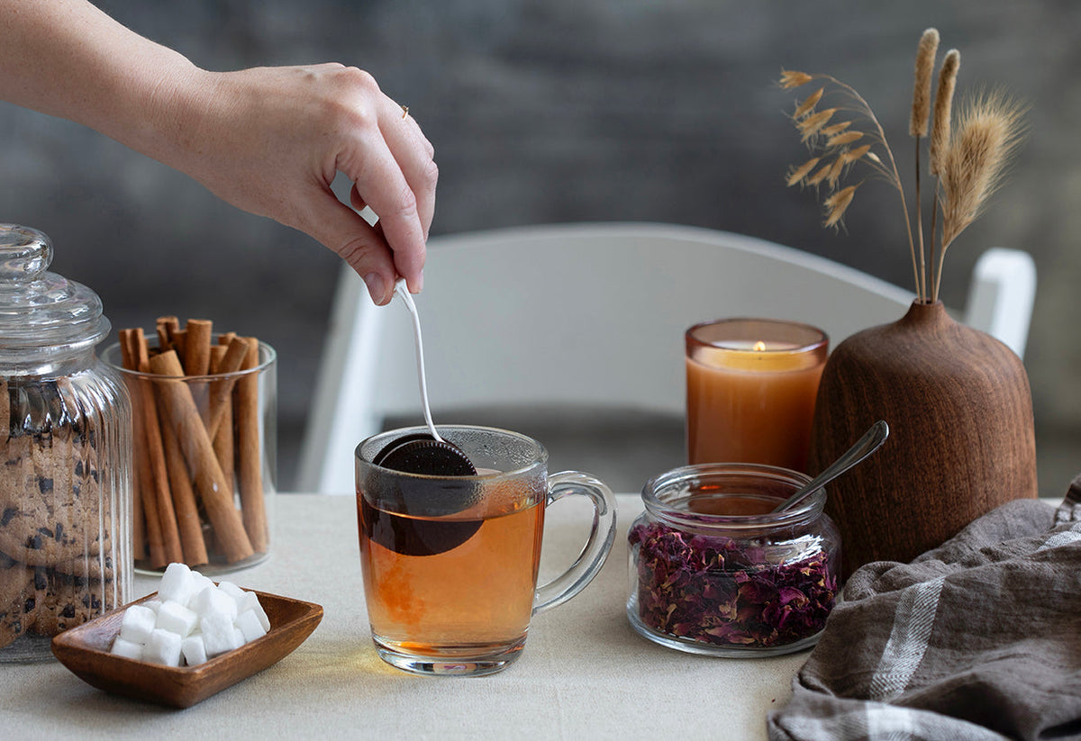 CookieTea theefilter in een mok thee op een sfeervol gedekte tafel met kaars en kaneelstokjes