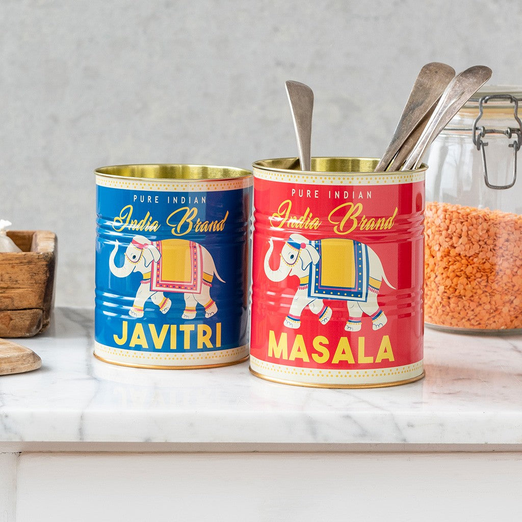 Rode blik Masala en blauwe blik Javitri met olifantopdruk op een marmeren aanrecht, met lepels in het rode blik en een glazen weckpot met rode linzen ernaast