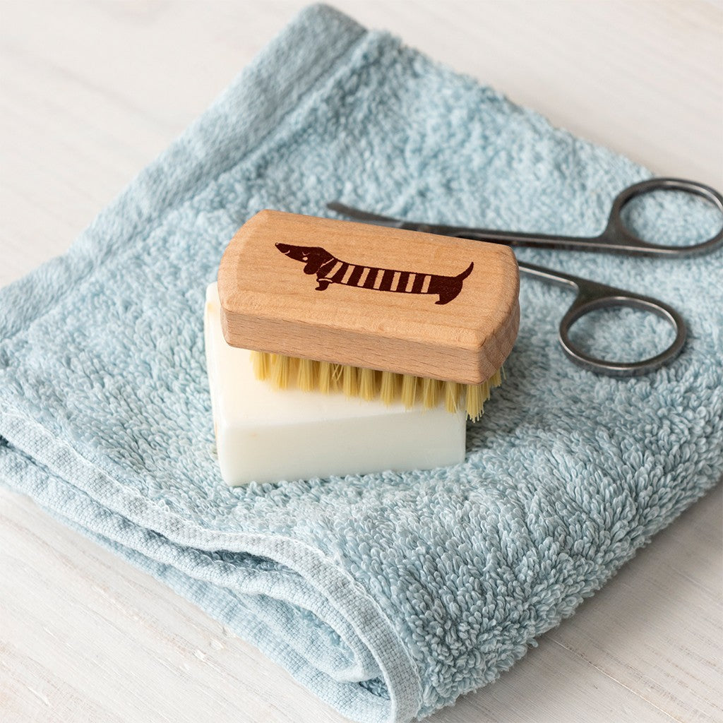 Houten nagelborstel met teckel op de rug op een stuk zeep, op een lichtblauwe handdoek naast een nagelschaartje