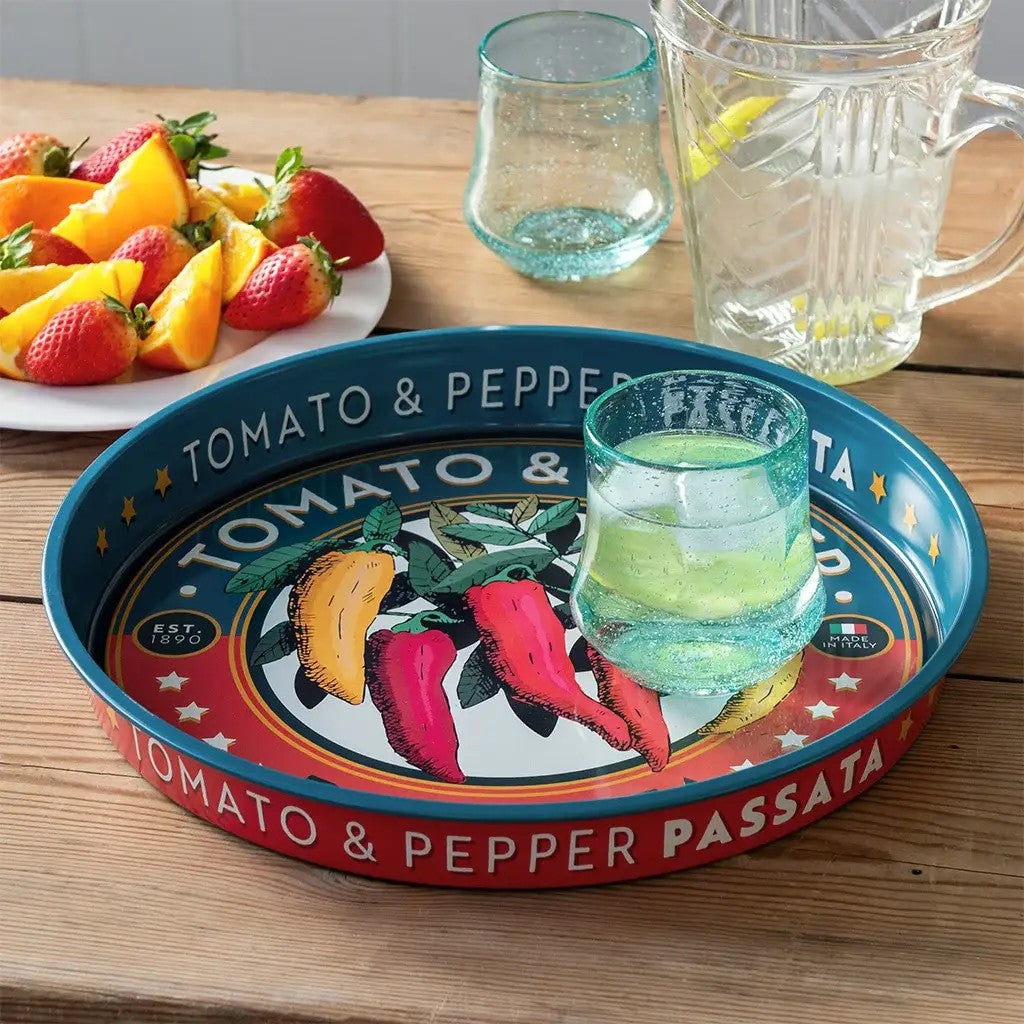 Dienblad met petrolblauwe rand en rode band op een houten tafel, met een glas water op het dienblad en ernaast een bord met aardbeien en sinaasappel en een glazen kan