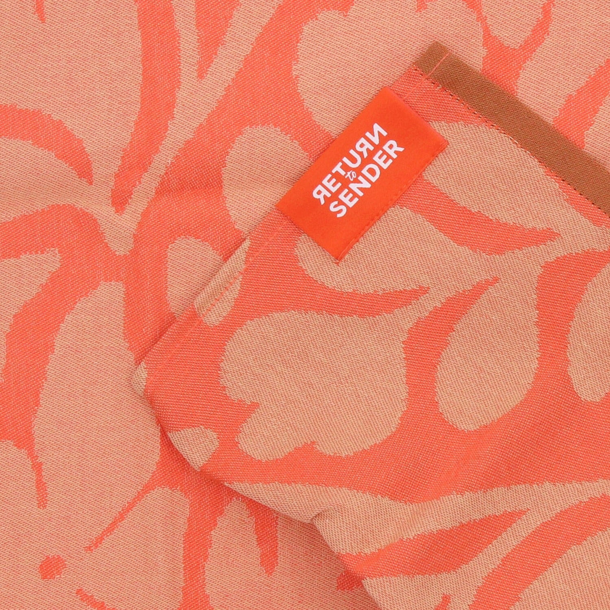 Theedoek Flower Carina - Coral, close-up van oranje label en bruine bies bij de omgeslagen hoek