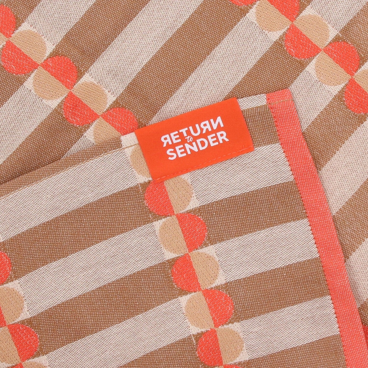 Theedoek Natural Ana - Coral, close-up van oranje label, koraalrode bies en halve cirkels op bruine strepen