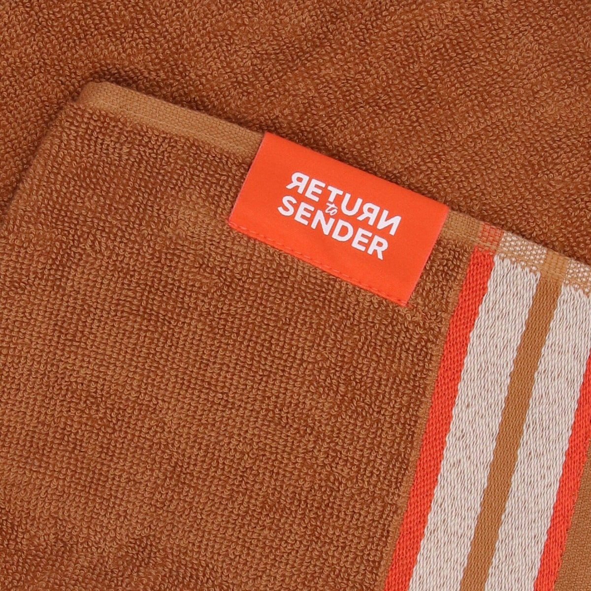 Keukendoek Sofia - Cashew, close-up van oranje Return to Sender-label op karamelbruine badstof naast de streepband
