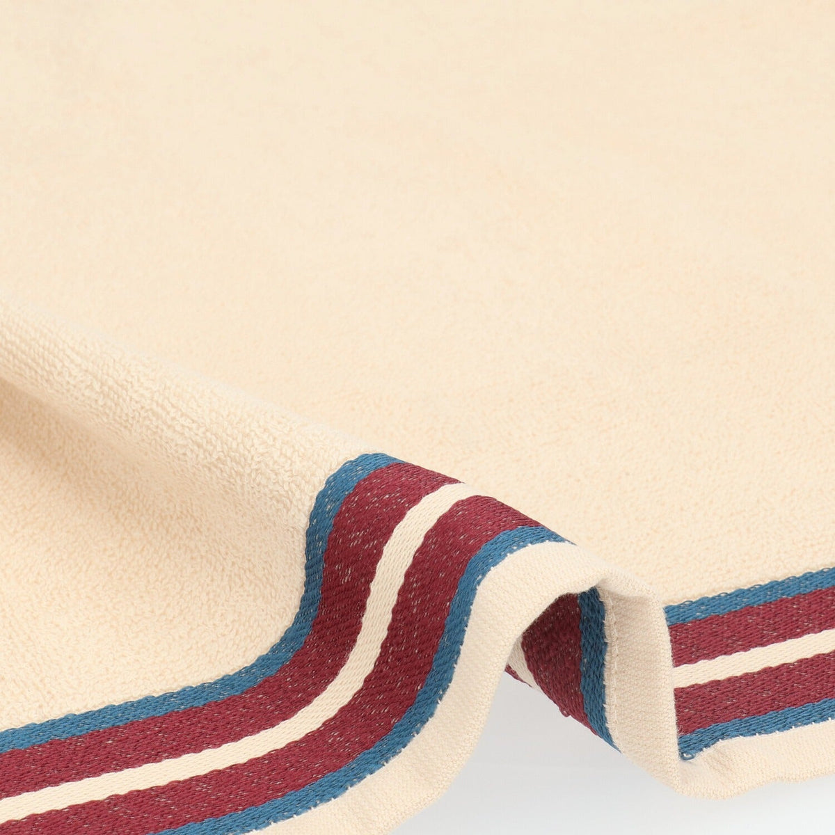 Keukendoek Ana - Soft Beige, close-up van crèmekleurige badstof en de bordeauxrode streepband met petrolblauwe randen