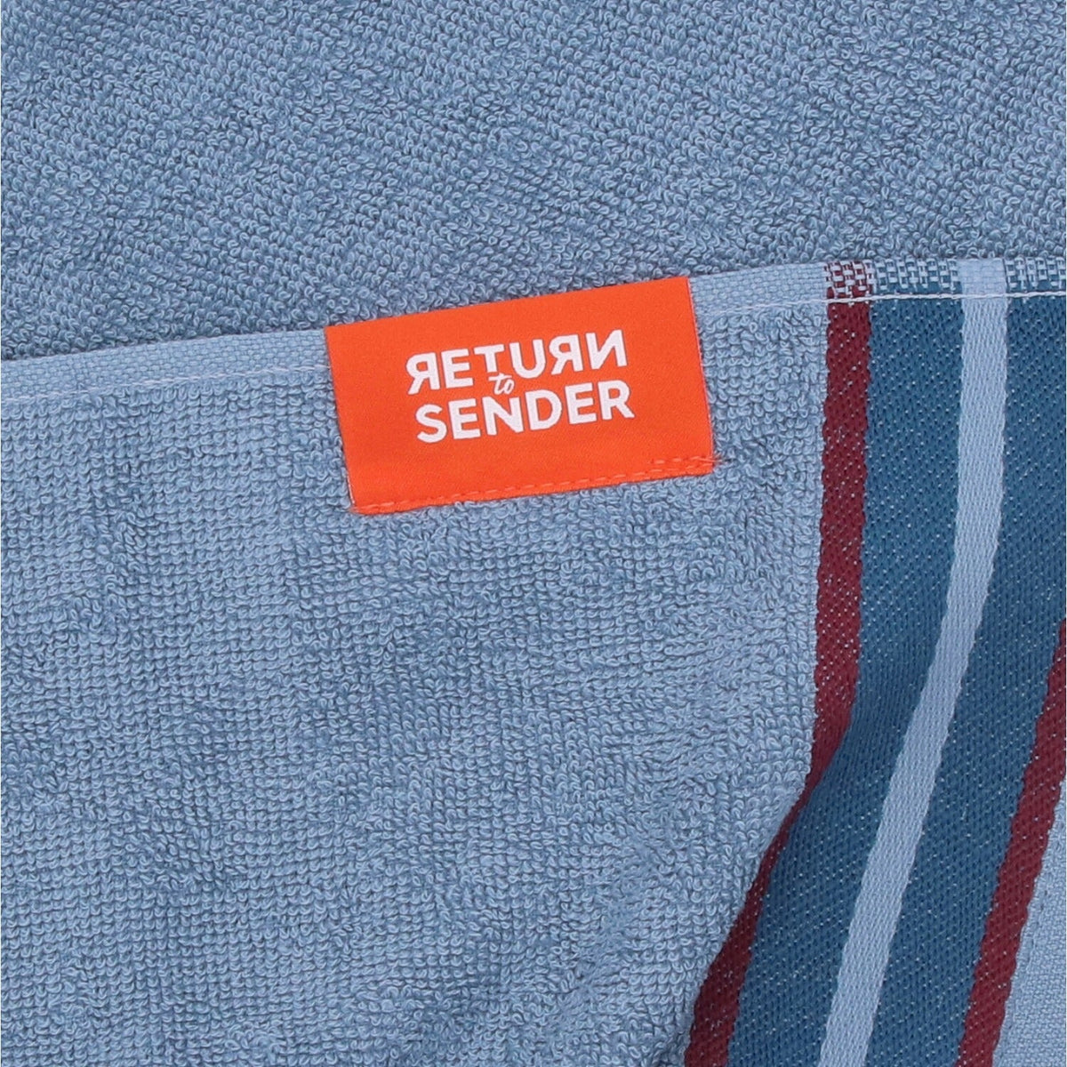 Keukendoek Sofia - Blue, close-up van oranje Return to Sender-label op blauwe badstof naast de streepband